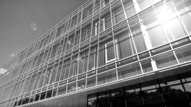 Gökyüzü arka planında cam cepheli modern ofis binası. Ofis binasının şeffaf cam duvarı. Gökyüzünde güneş ışığı olan güneşli bir gün. Siyah ve beyaz.