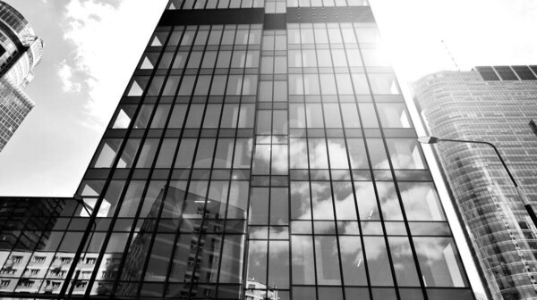 Modern office building with glass facade on a clear sky background. Transparent glass wall of office building. Bright sunny day with sunbeams on the sky. Black and white.