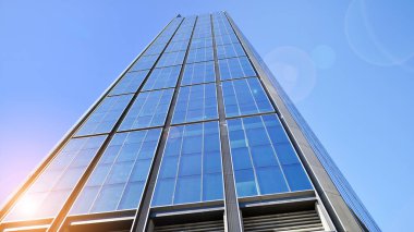 Mavi gökyüzüne karşı modern gökdelenin alt manzarası. Şehir merkezindeki iş binalarına bakıyorum. Ufukta yükselen güneş.