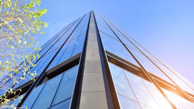 Mavi gökyüzüne karşı modern gökdelenin alt manzarası. Şehir merkezindeki iş binalarına bakıyorum. Ufukta yükselen güneş.