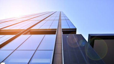 Bottom view of modern skyscraper in business district against blue sky. Looking up at business buildings in downtown. Rising sun on the horizon.