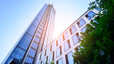 Mavi gökyüzüne karşı modern gökdelenin alt manzarası. Şehir merkezindeki iş binalarına bakıyorum. Ufukta yükselen güneş.