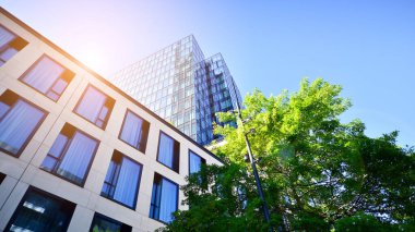 Mavi gökyüzüne karşı modern gökdelenin alt manzarası. Şehir merkezindeki iş binalarına bakıyorum. Ufukta yükselen güneş.