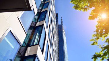 Mavi gökyüzüne karşı modern gökdelenin alt manzarası. Şehir merkezindeki iş binalarına bakıyorum. Ufukta yükselen güneş.