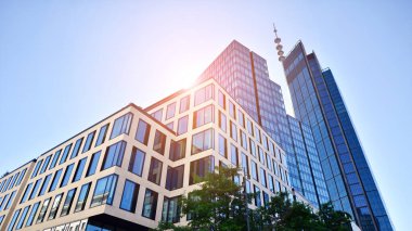 Mavi gökyüzüne karşı modern gökdelenin alt manzarası. Şehir merkezindeki iş binalarına bakıyorum. Ufukta yükselen güneş.