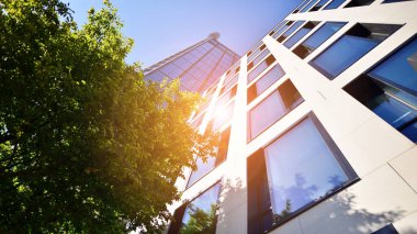 Mavi gökyüzüne karşı modern gökdelenin alt manzarası. Şehir merkezindeki iş binalarına bakıyorum. Ufukta yükselen güneş.