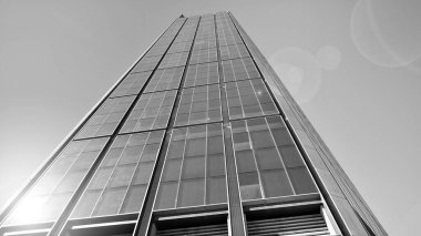 Mavi gökyüzüne karşı modern gökdelenin alt manzarası. Şehir merkezindeki iş binalarına bakıyorum. Ufukta doğan güneş. Siyah ve beyaz.