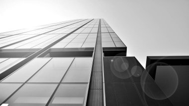 Mavi gökyüzüne karşı modern gökdelenin alt manzarası. Şehir merkezindeki iş binalarına bakıyorum. Ufukta doğan güneş. Siyah ve beyaz.