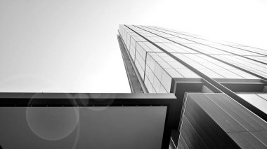 Mavi gökyüzüne karşı modern gökdelenin alt manzarası. Şehir merkezindeki iş binalarına bakıyorum. Ufukta doğan güneş. Siyah ve beyaz.