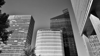 Bottom view of modern skyscraper in business district against blue sky. Looking up at business buildings in downtown. Rising sun on the horizon. Black and white.
