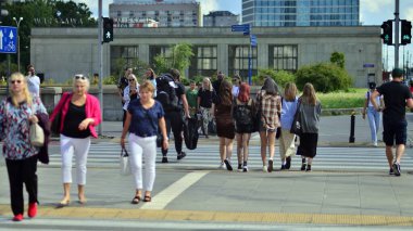 Warsaw, Poland. 10 August 2022. People of different ages and with comfortable clothes crossing the road through. View of a city street with residents, tourists and buildings.