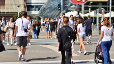 Warsaw, Poland. 10 August 2022. People of different ages and with comfortable clothes crossing the road through. View of a city street with residents, tourists and buildings.