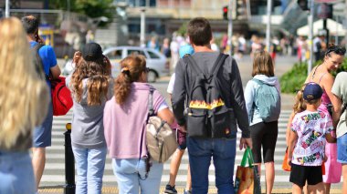 Warsaw, Poland. 10 August 2022. People of different ages and with comfortable clothes crossing the road through. View of a city street with residents, tourists and buildings.