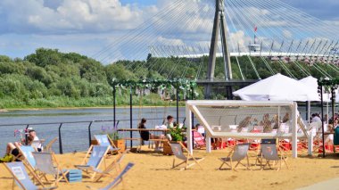 Warsaw Poland. August 10, 2022. Vistula Boulevards. Customers enjoy the holiday weather and take advantage of the many restaurant gardens with sand, sun loungers and large umbrellas.