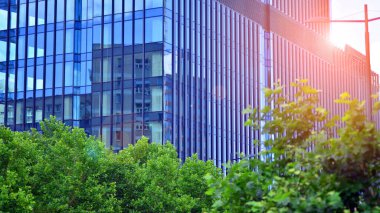 Mavi gökyüzüne karşı modern cam cephe. İş bölgesindeki bir binanın alt manzarası. Bir ofis binasının cam cephesinin alçak açılı görüntüsü.