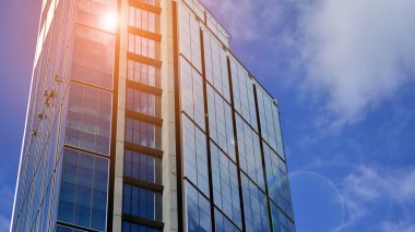 Mavi gökyüzüne karşı modern cam cephe. İş bölgesindeki bir binanın alt manzarası. Bir ofis binasının cam cephesinin alçak açılı görüntüsü.