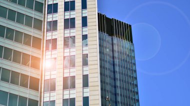 Mavi gökyüzüne karşı modern cam cephe. İş bölgesindeki bir binanın alt manzarası. Bir ofis binasının cam cephesinin alçak açılı görüntüsü.