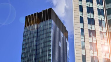 Mavi gökyüzüne karşı modern cam cephe. İş bölgesindeki bir binanın alt manzarası. Bir ofis binasının cam cephesinin alçak açılı görüntüsü.