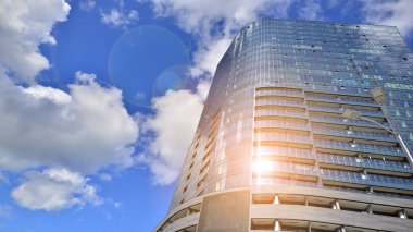 Mavi gökyüzüne karşı modern gökdelenin alt manzarası. Şehir merkezindeki iş binalarına bakıyorum. Ufukta yükselen güneş.