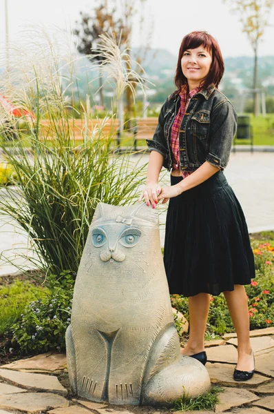 Ung kvinna som står nära rolig katt staty — Stockfoto