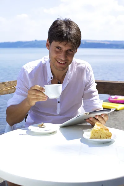 Glücklicher Mann lächelt beim Frühstück am See mit Tablette — Stockfoto