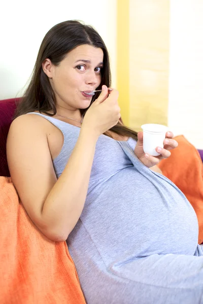 Felice donna incinta mangiare yogurt a casa Foto Stock