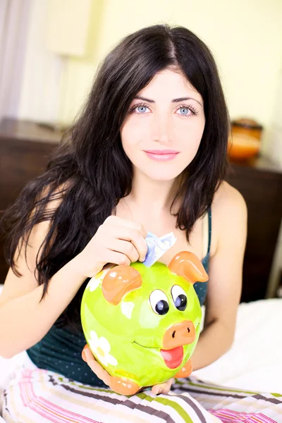 Happy woman putting money in piggy bank — Stock Photo, Image