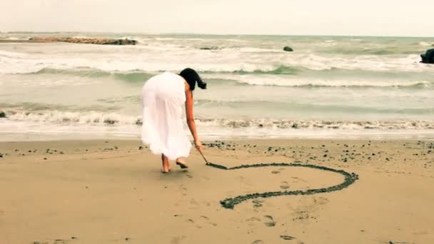 Beautiful woman making love sign on the sand for her boyfriend smiling — Stock Video