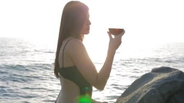 Sahilde günbatımı sırasında şarap kırmızı cam kadınla