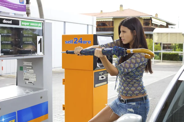 Woman trying to destroy gas station with umbrella — Stock Photo, Image