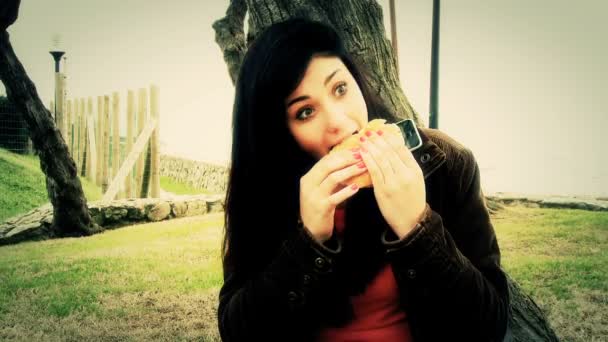 Menina comendo hambúrguer com telefone celular — Vídeo de Stock