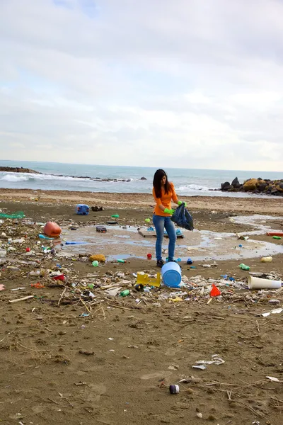 Plage pleine de saleté et de décharge avec une jeune femme essayant de nettoyer — Photo