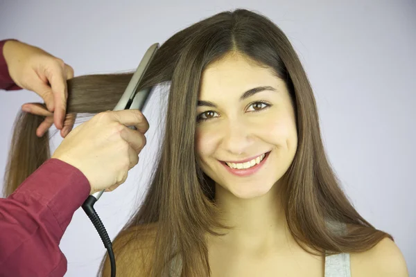 Professional hair dresser ironing long hair of cute smiling woman — Stock Photo, Image