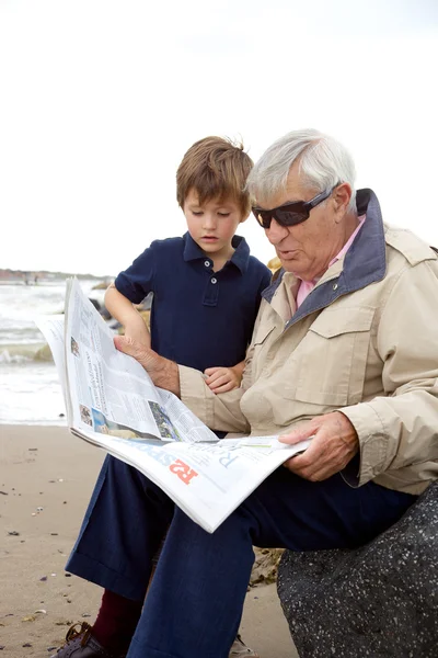 Little boy looking newspaper with grandpa — Stock Photo, Image