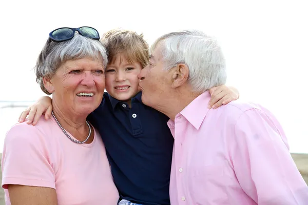 Criança feliz sendo beijada pelo avô e abraçada pela avó — Fotografia de Stock