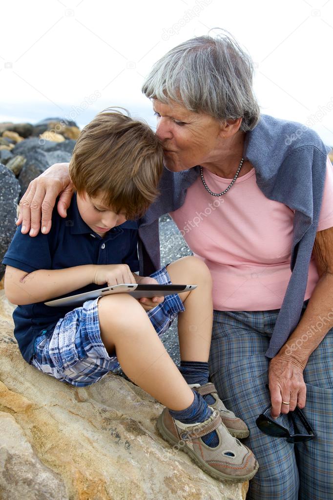 Grandma kissing with love grandson playing with tablet on the beach