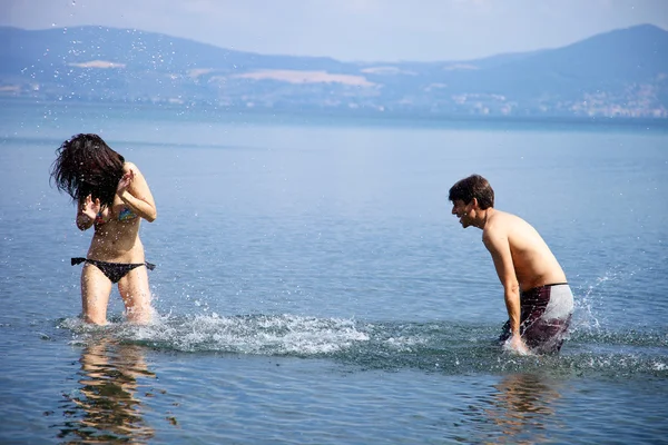 Happy couple in vacation splashing water at each other — Stock Photo, Image