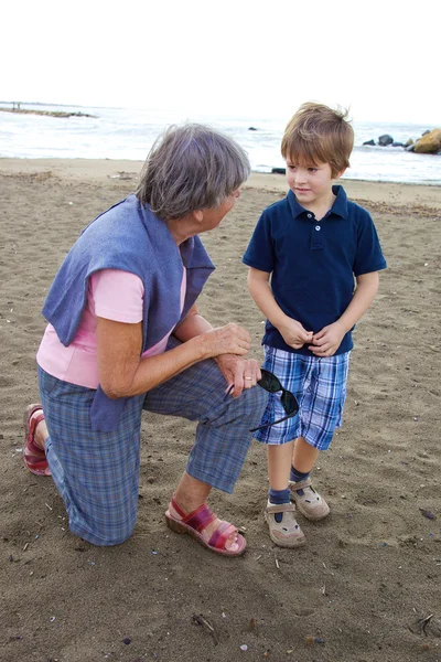 Happy grandmother chatting with grandson on a beach — Stock Photo, Image