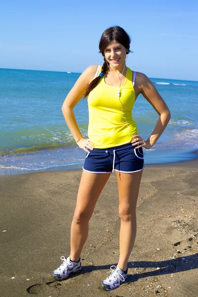 Mutlu sportif kadın gülümseyerek plaj üzerinde müzik dinleme — Stok fotoğraf