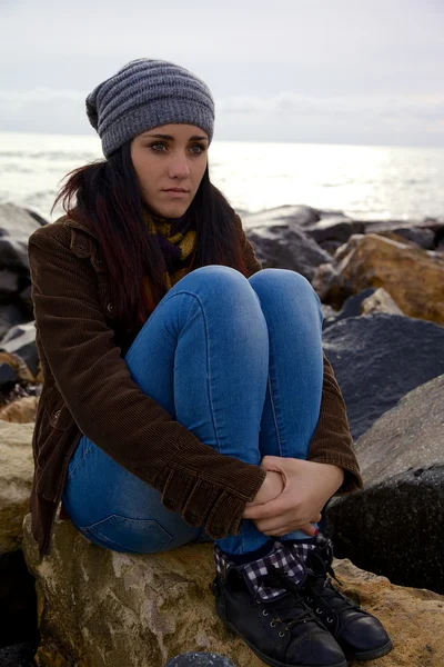 Cute young woman thinking feeling emotion on rocks in front of the sea — Stock Photo, Image