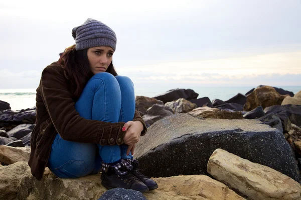 Kışın okyanusun önünde oturan üzgün genç kadın — Stok fotoğraf