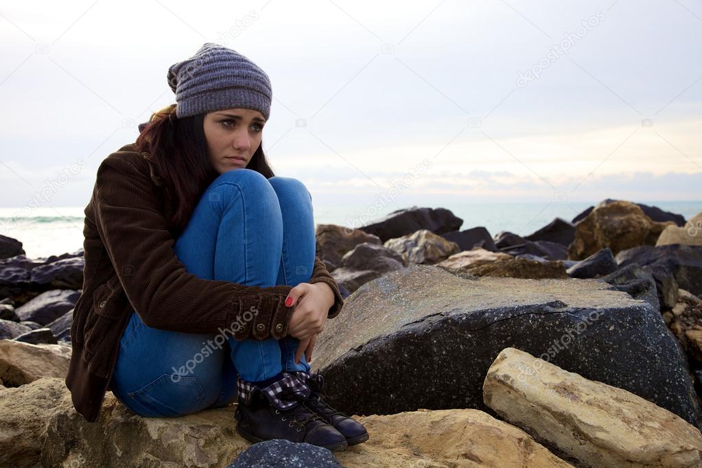 Sad young woman sitting in front of the ocean in the winter