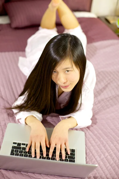快乐的亚洲女孩躺在床上与 pc 机 — 图库照片