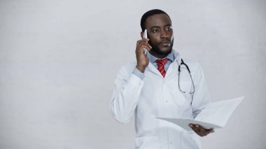 Dosyaları elinde tutarken akıllı telefondan konuşan Afrikalı Amerikalı doktor.
