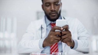Bulanık Afro-Amerikan doktor akıllı telefondan mesaj atıyor. 