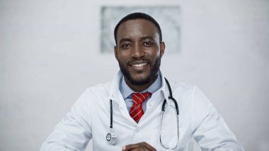 Steteskoplu mutlu Afro-Amerikan doktor kameraya bakıyor.