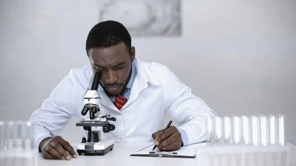Scienziato Afroamericano Che Guarda Attraverso Microscopio Scrive Negli Appunti — Foto Stock