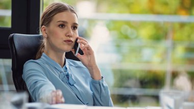 Düşünceli iş kadını iş yerinde otururken cep telefonundan arıyor