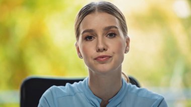 Genç ve ciddi iş kadını ofiste kameraya bakıyor.