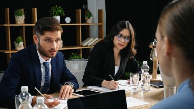 Genç adam, iş kadınının yanındaki bulanık meslektaşıyla konuşuyor. Not defterine yazıyor.